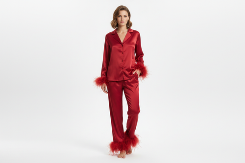 FEMME BLANCHE DEBOUT EN STUDIO AVEC ENSEMBLE DE PYJAMA SATINE ELEGANT ROUGE AVEC BOUTON AVEC PLUME SUR LES MANCHETTE ET USR LE BAS DU PANTALON