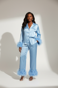 FEMME NOIR DEBOUT EN STUDIO AVEC ENSEMBLE DE PYJAMA SATINE ELEGANT BLEU CIEL AVEC BOUTON AVEC PLUME SUR LES MANCHETTE ET SUR LE BAS DU PANTALON